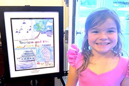 Destin Elementary School kindergartner Claire Grelle smiles beside her framed award-winning artwork during a student recognition event.