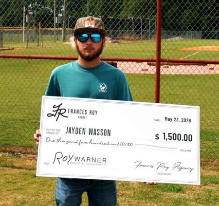 Baker High School graduate Jayden Wasson holds a ceremonial $1,500 Roy Warner Memorial Scholarship check from Frances Roy Agency at a baseball field.