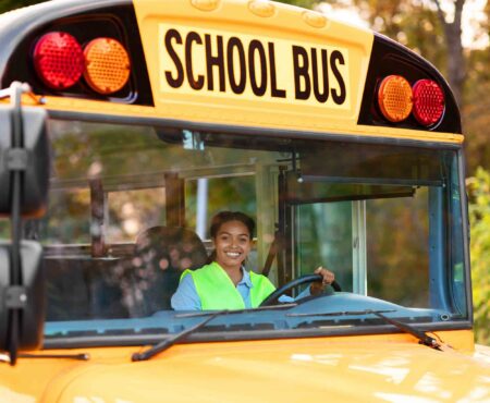 School bus driver seated behind the wheel of a yellow school bus.