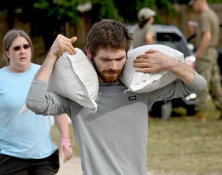 Man carries two sandbags over his shoulders as residents prepare for approaching hurricane conditions.