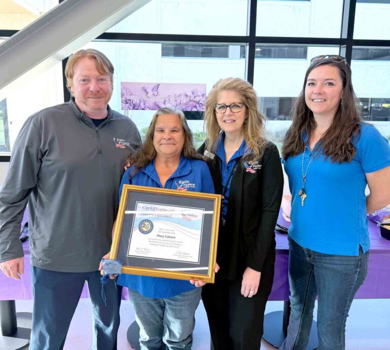 Eglin Federal Credit Union employees celebrate Mary Calvert’s 25 years of service as she holds a framed certificate of achievement.